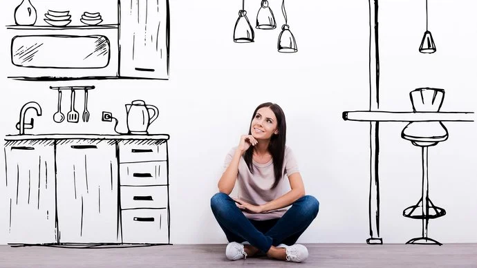 Eine Frau sitzt vor einer weißen Wand, auf die eine Küche gezeichnet ist