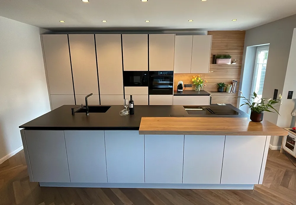 Moderne mattgraue Küche mit Kochinsel mit Arbeitsplatten aus schwarzem Stein und Holzakzenten