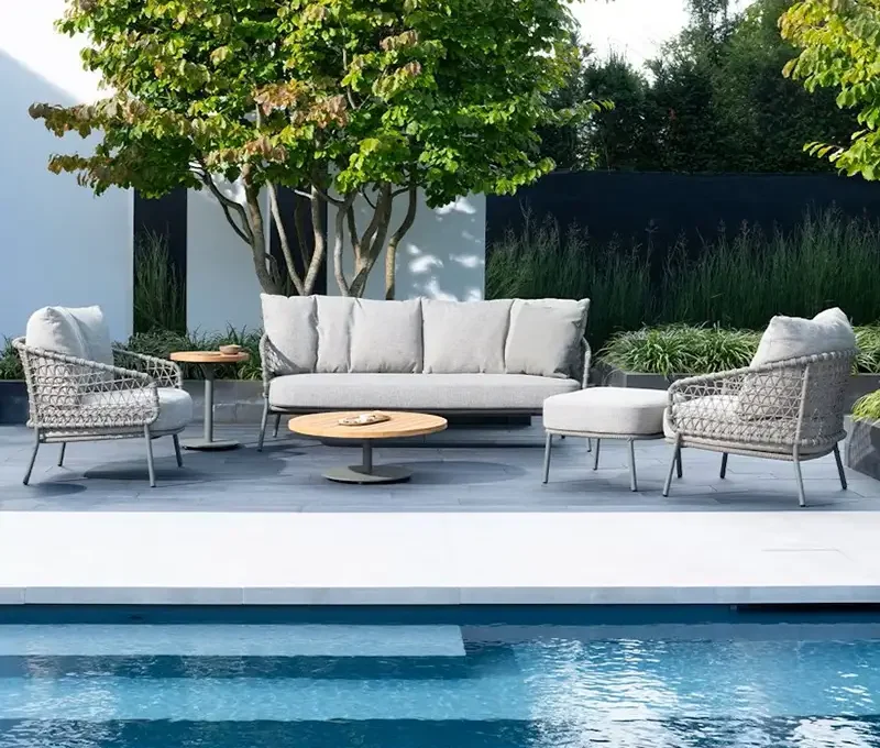 Gartenmöbel stehen am Pool vor einem prächtigen Garten