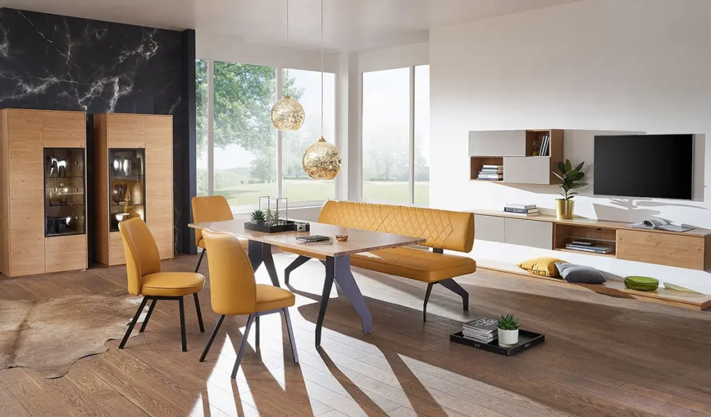 Wohnen - Esstisch mit Holzplatte auf Metallbeinen mit einer Lederbank und drei orangefarbenen Stuehlen mit TV-Staender