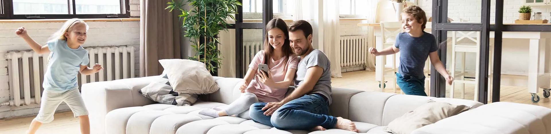 Zwei Erwachsene sitzen glücklich auf dem Sofa und zwei Kinder toben in der Nähe