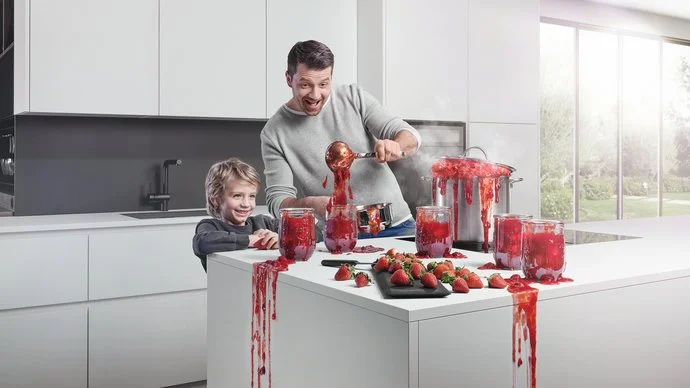 Vater und Sohn in weißer Küche beim Marmelade-Einkochen, alles tropft und spritzt