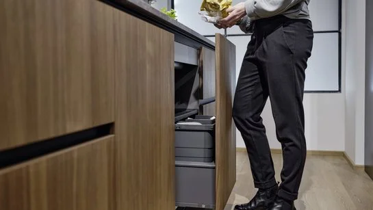 Frau in der Küche mit Abfall in der Hand vor Unterschrank mit automatischem Müllsystem