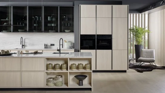 Inselküche in eiche weiß mit Glasoberschränken, daneben ein Wohnzimmer