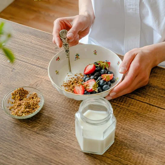Jemand bereitet auf einer Arbeitsplatte aus Holz Müsli mit Früchten zu