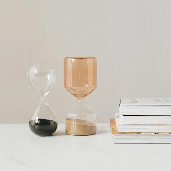 Zwei große Sanduhren stehen nebeneinander, daneben liegen Bücher