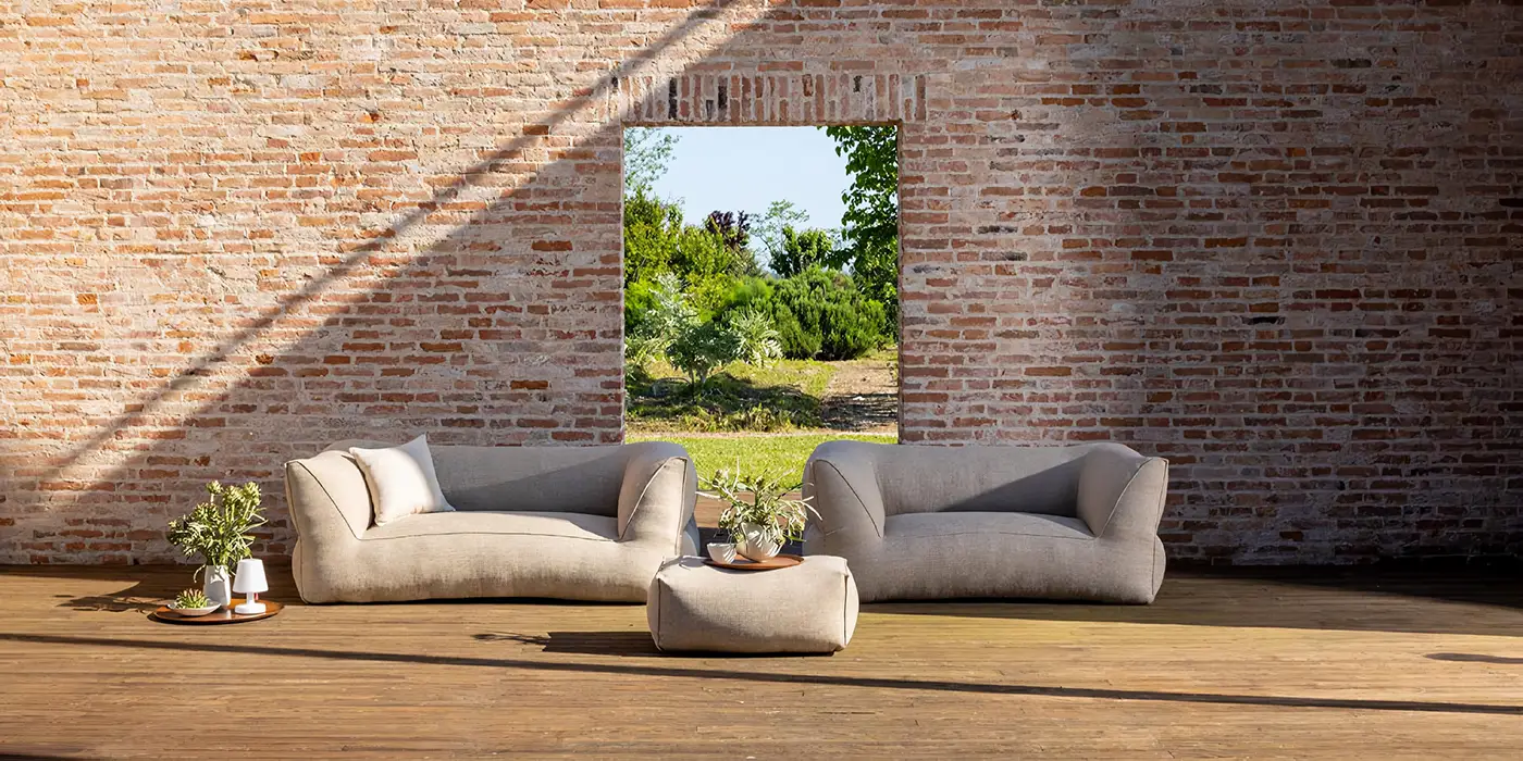 Zwei weiche Sofas und ein Pouf stehen auf einer Terrasse vor einer Ziegelwand